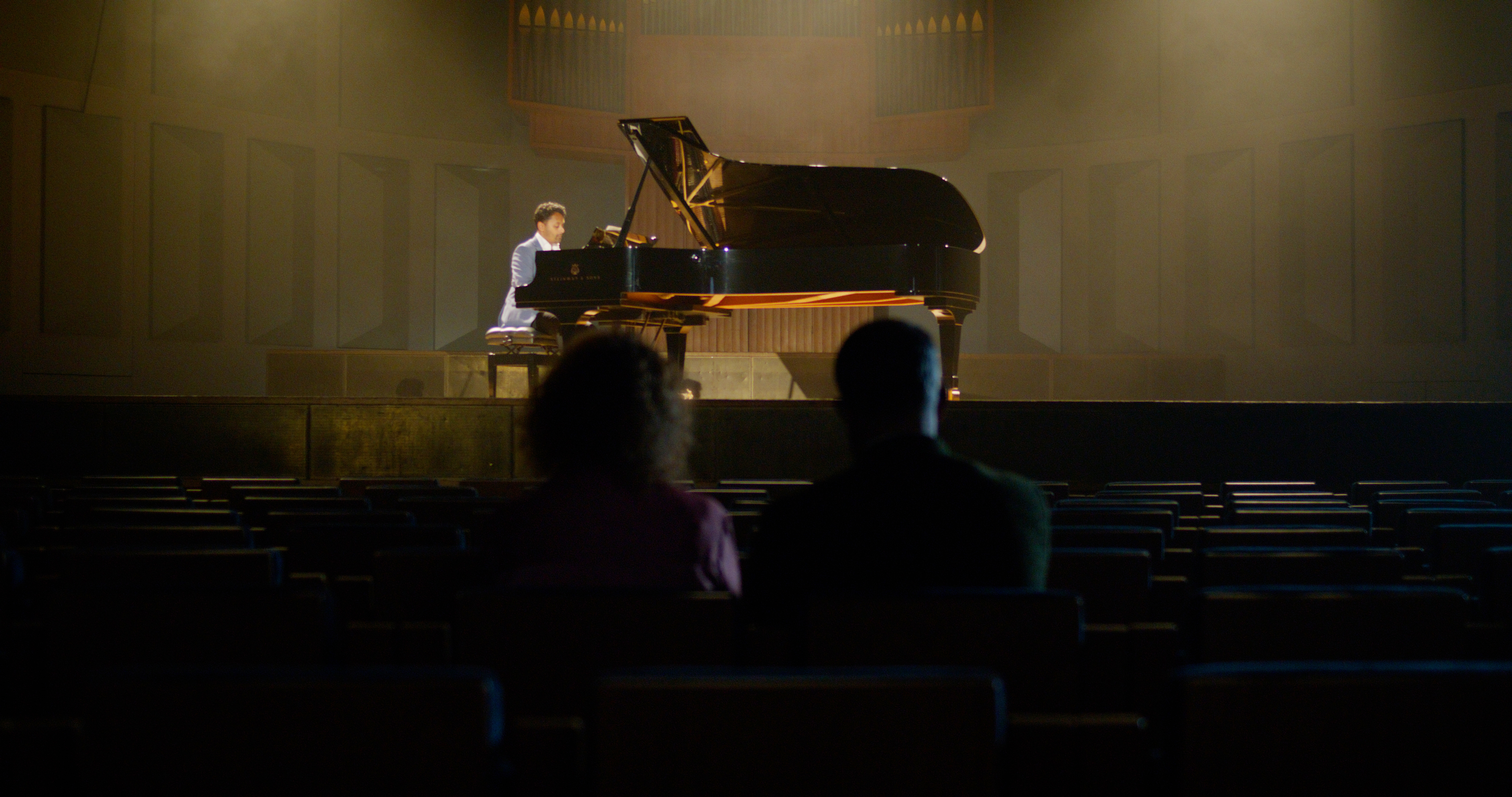 Two people in the audience watching piano player on stage
